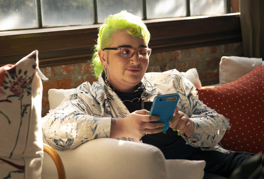 A queer person with green hair works on their mobile deviece