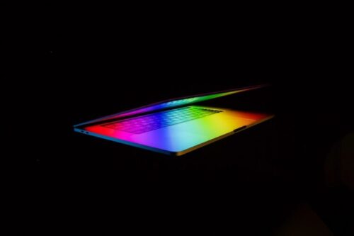 A laptop partially open emitting a rainbow glow on the keyboard.